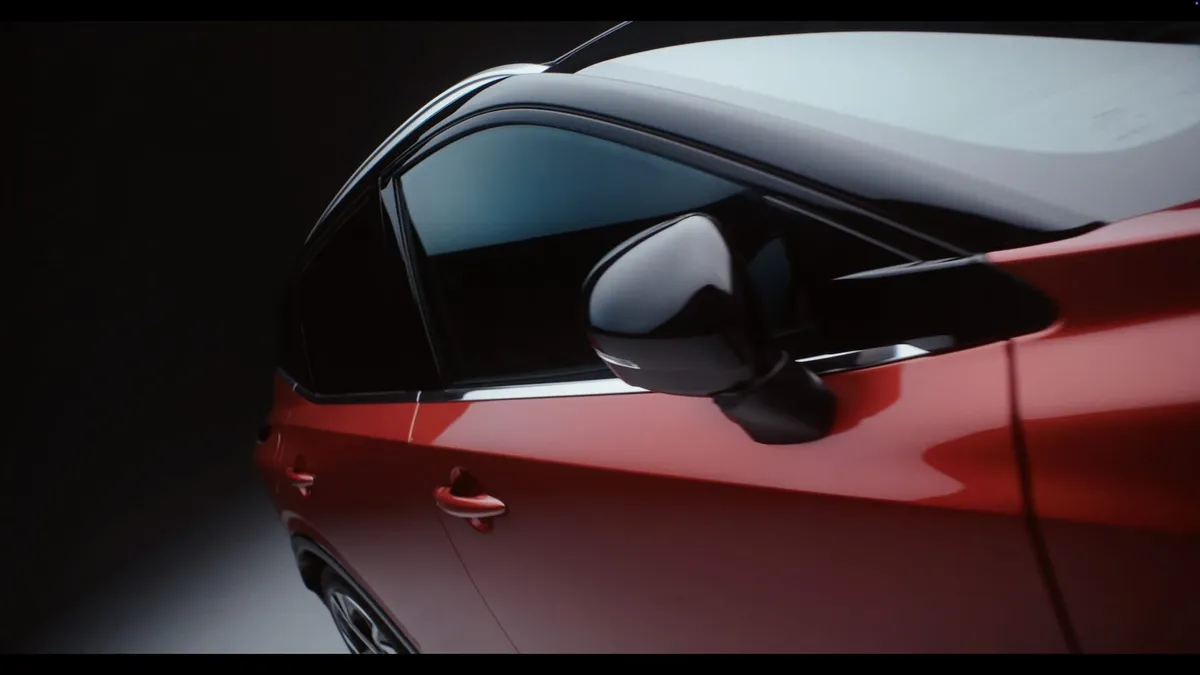 Close-up of a red car's wing mirror and door handle, dark tinted window and white roof reflecting light in a studio setting.